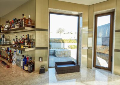 A well-stocked, modern home bar with a variety of spirits on glass shelves and natural light coming in through windows.