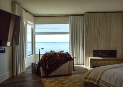 Modern bedroom with ocean view, featuring a fur throw on a bench and sheer curtains.