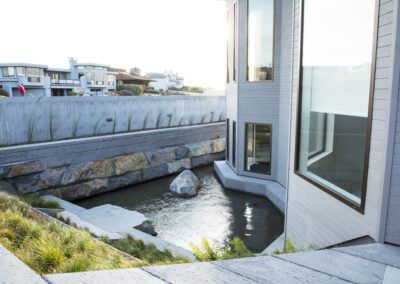 Modern residential architecture featuring a water channel with rocks along a grassy landscape.